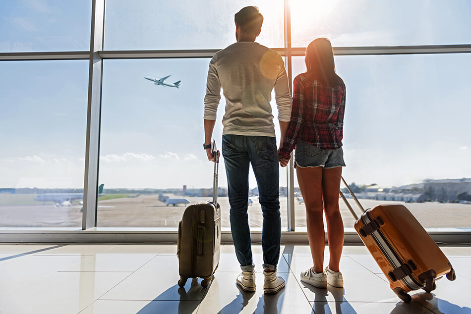 man and woman with suitcases in an airport watching a plane take off