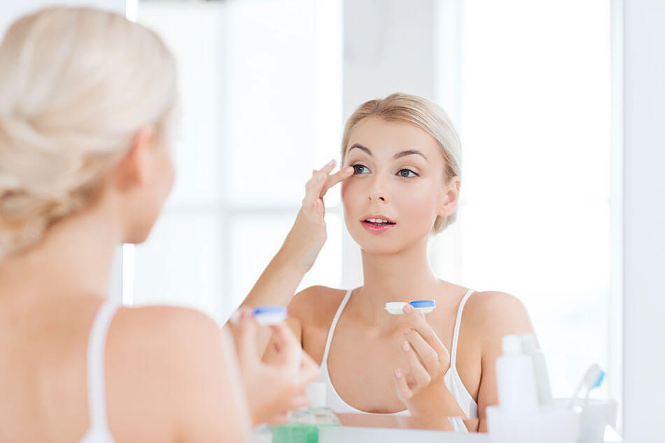 blonde woman putting contacts in mirror