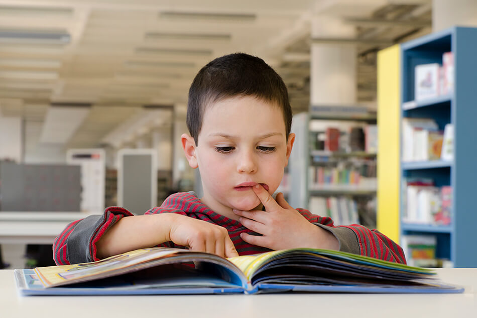 boy reading a book with one finger in his mouth and one on a page