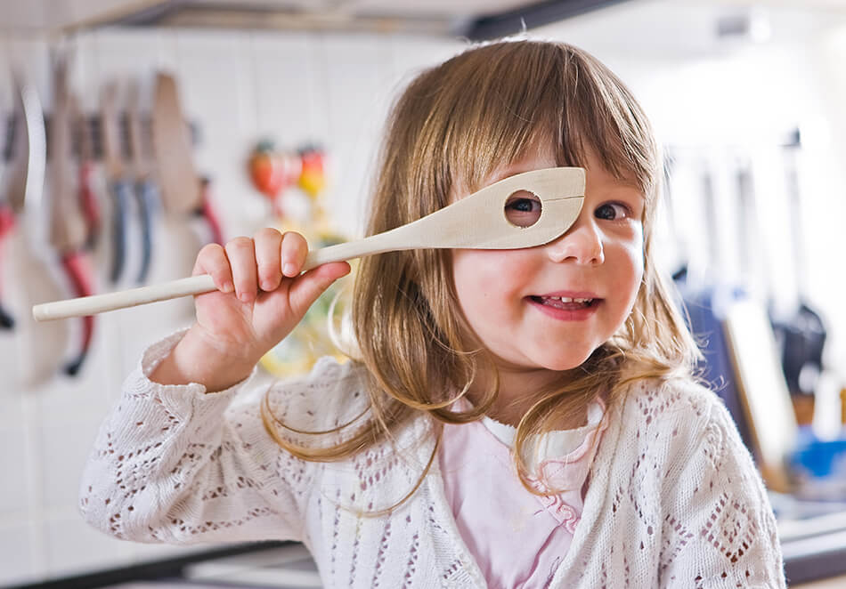 child looking through wooden spoon she’s holding up to her eye