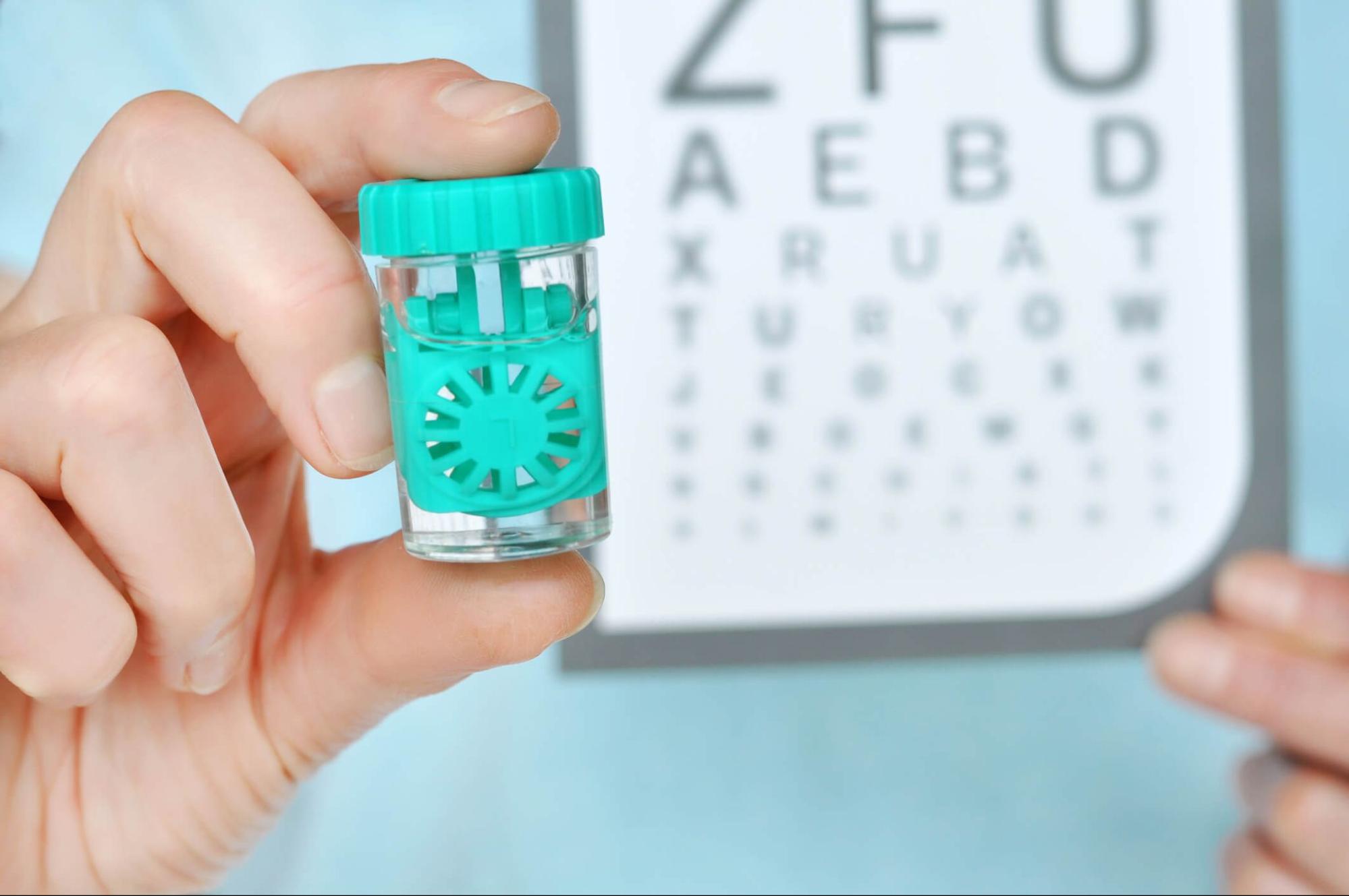 Contact lens case held up in front of an eye exam chart