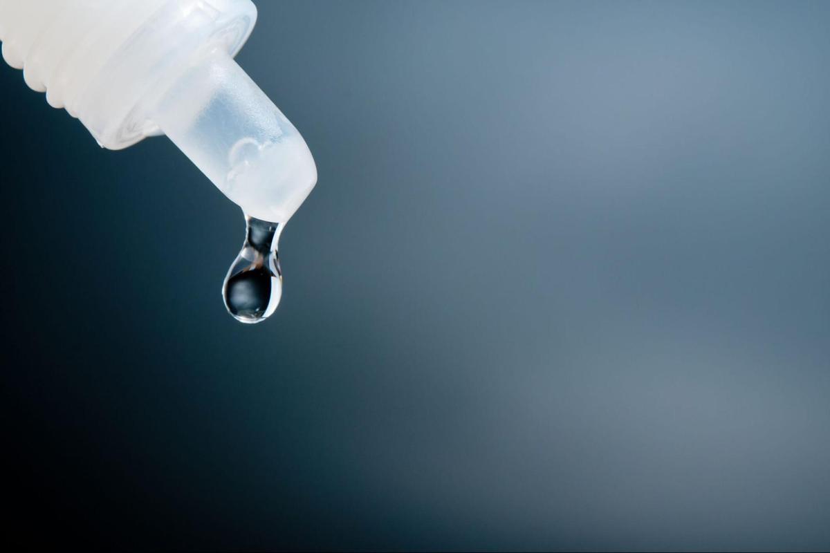Close-up of eye drops dripping from a bottle, representing contact lens care and eye hydration