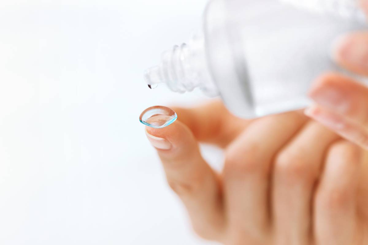 contact lens on fingertip with contact lens solution dripping in