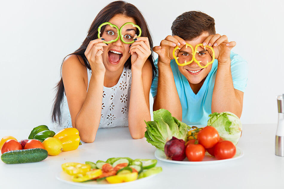 couple with plates of vegetables holding pepper slices up to their eyes