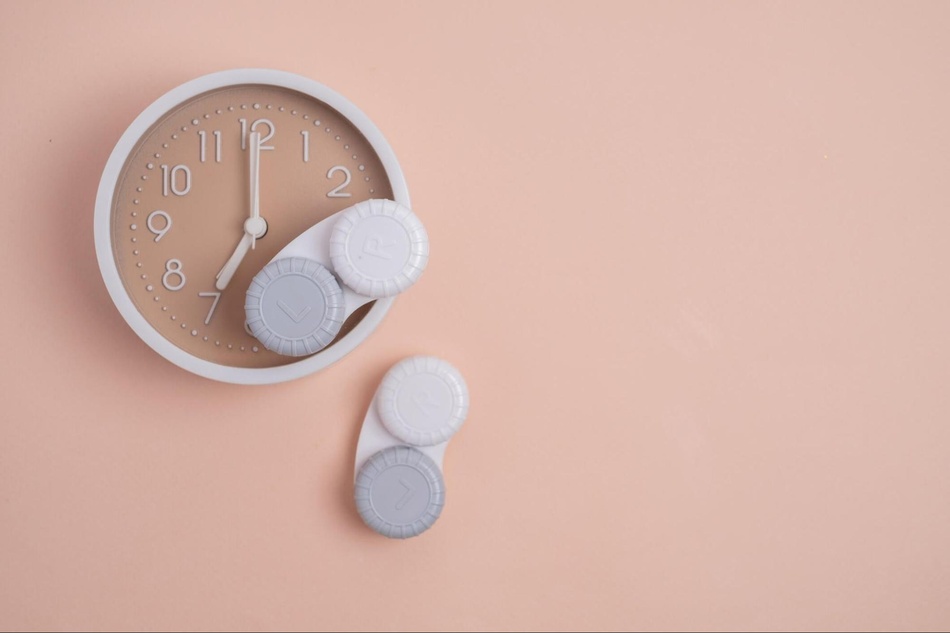 Contact lens cases next to an alarm clock_daily and monthly contact lens care routine