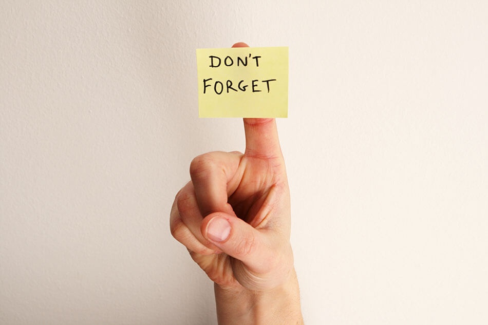 Hand holding a sticky note with “Don’t Forget” written on it
