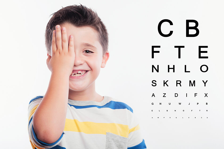 boy covering one eye beside exam chart