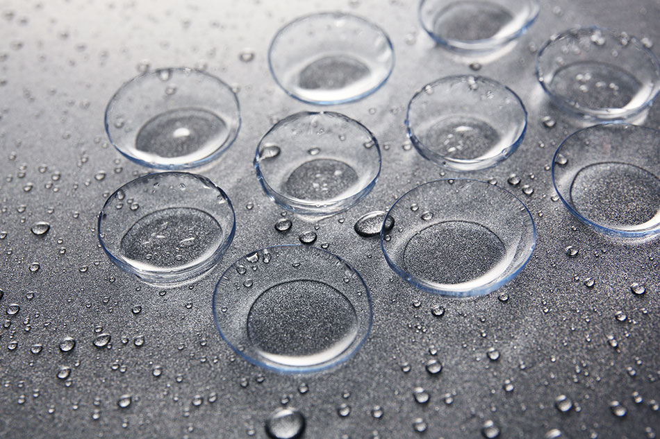 Different types of contact lenses with water drops on gray table