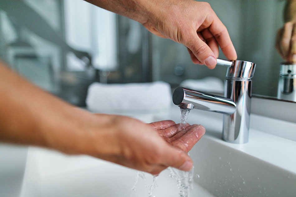 man holding hand under water flow from faucet