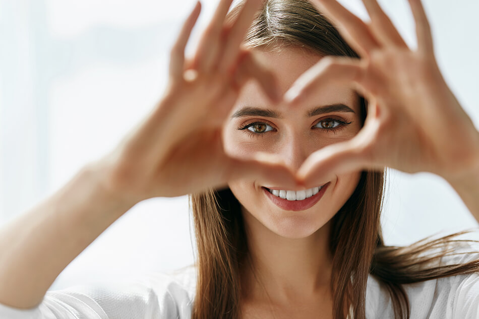 woman framing her eyes inside a heart she’s making with her hands