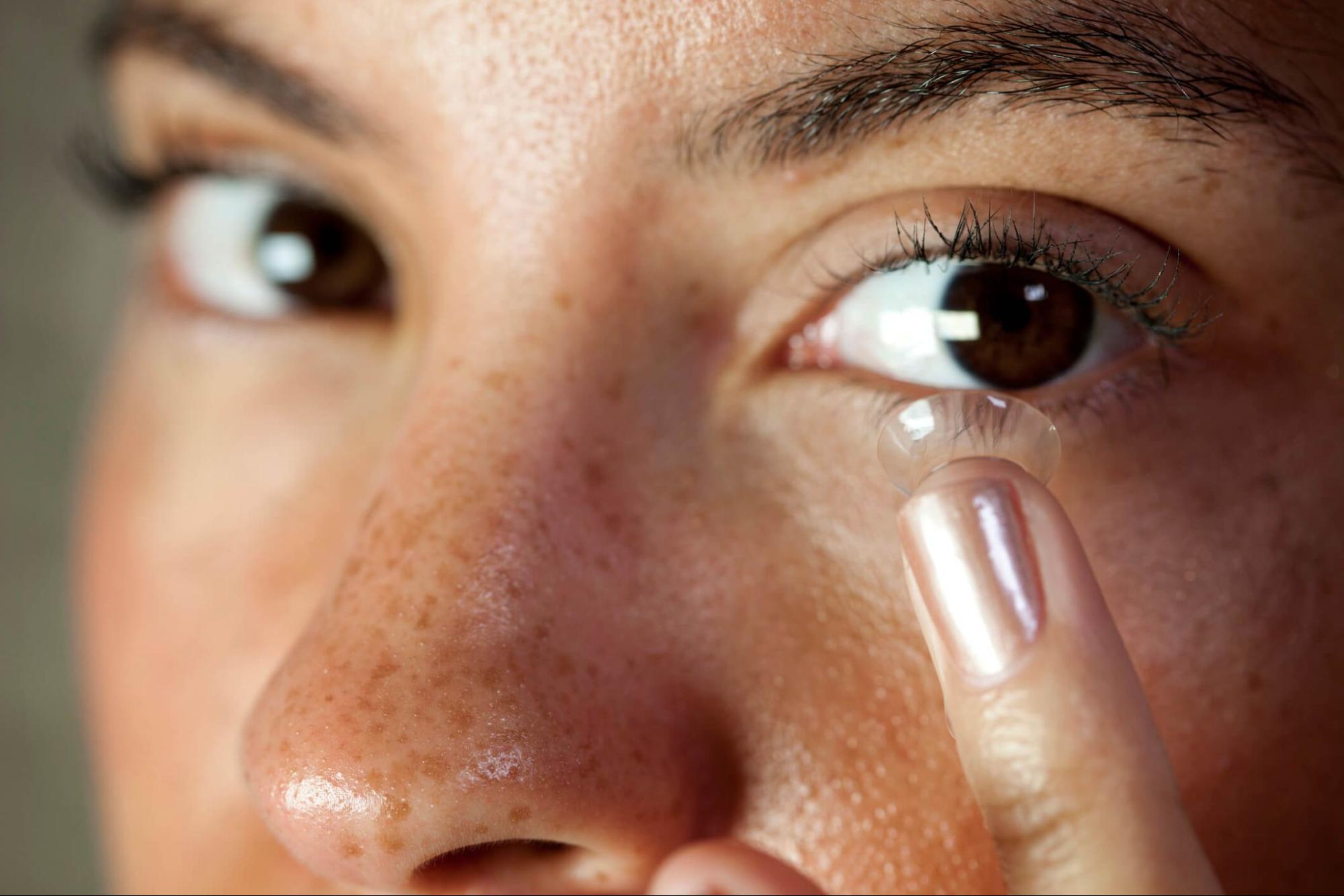 Close-up of a person inserting a contact lens with clean hands as part of daily contact lens care