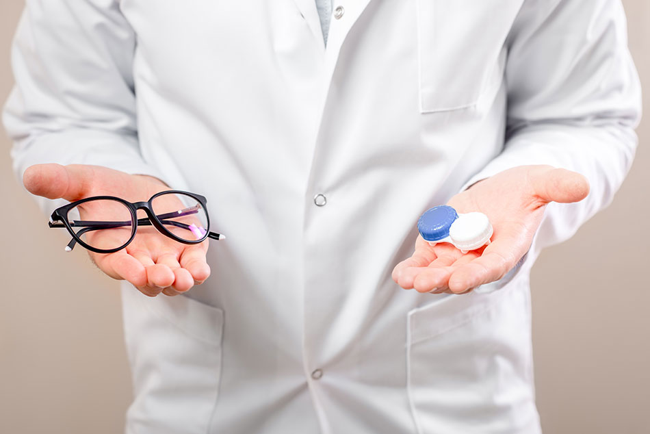 Male eye doctor holding glasses in one hand and contacts case in the other