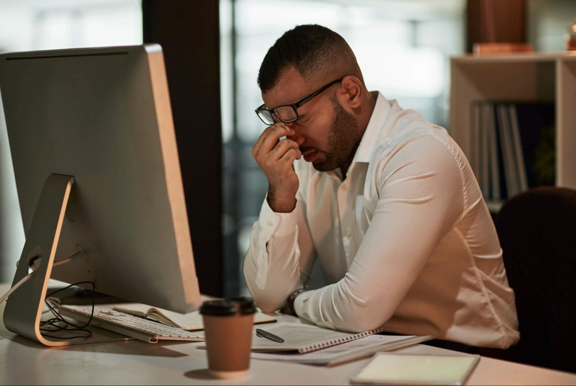 Man with eye strain wearing reading glasses at computer