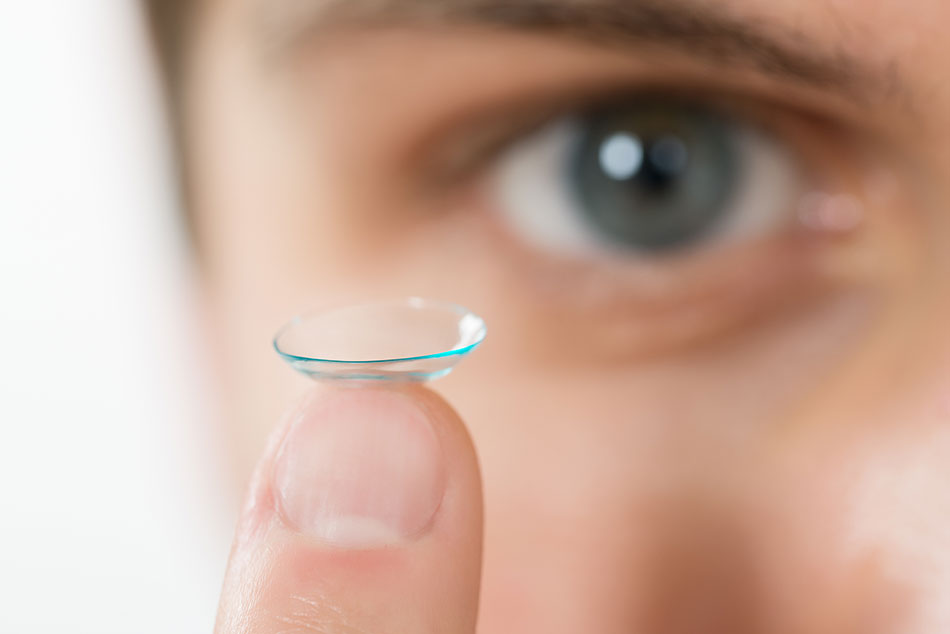 close-up of man eyeing the contact lens on the tip of his finger