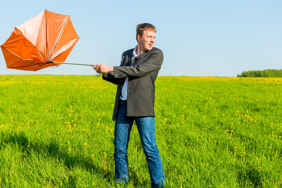 man fighting wind with umbrella blown back