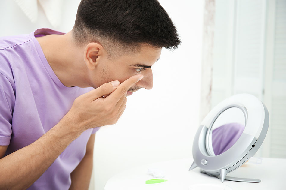 young man putting in contact lens in front of tabletop mirror