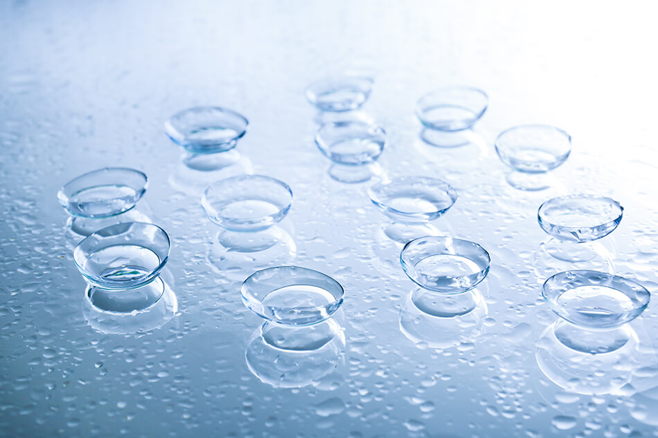 several daily and weekly contact lenses on a blue mirrored surface