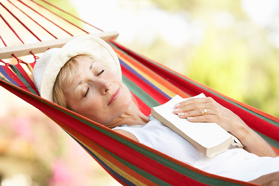 Older woman sleeping in hammock with book