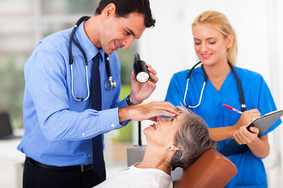 Ophthalmologist examining senior woman’s eye with light