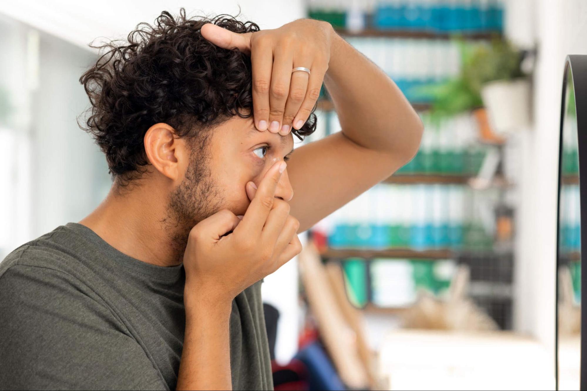 Man putting in contact lenses while pulling eyelid and looking in mirror