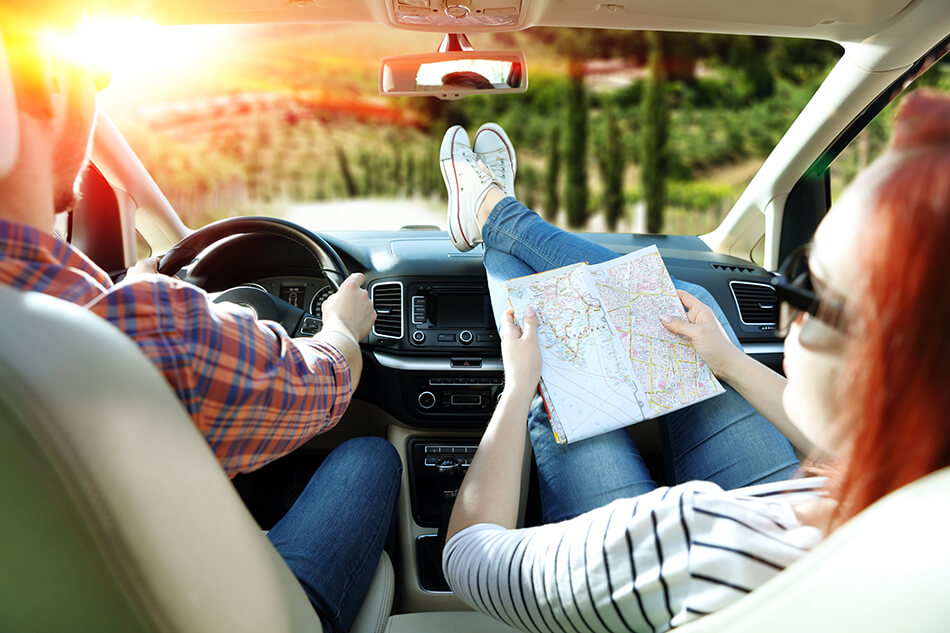 man driving a car while woman is relaxed and looking at road map