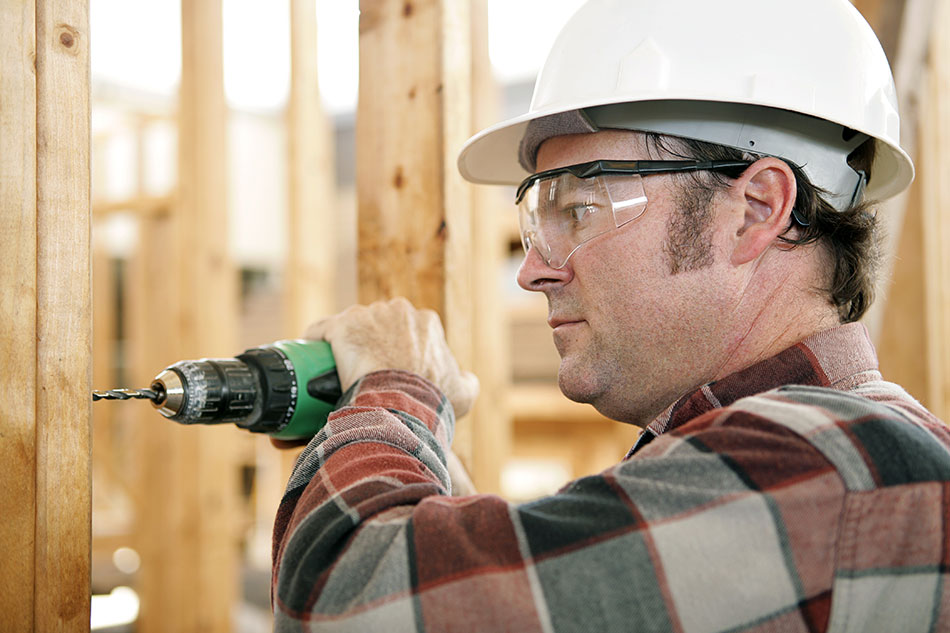 man wearing safety goggles and white helmet while using a drill