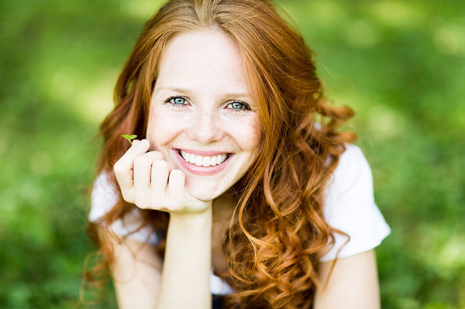 Smiling red-haired woman lying on grass outdoors