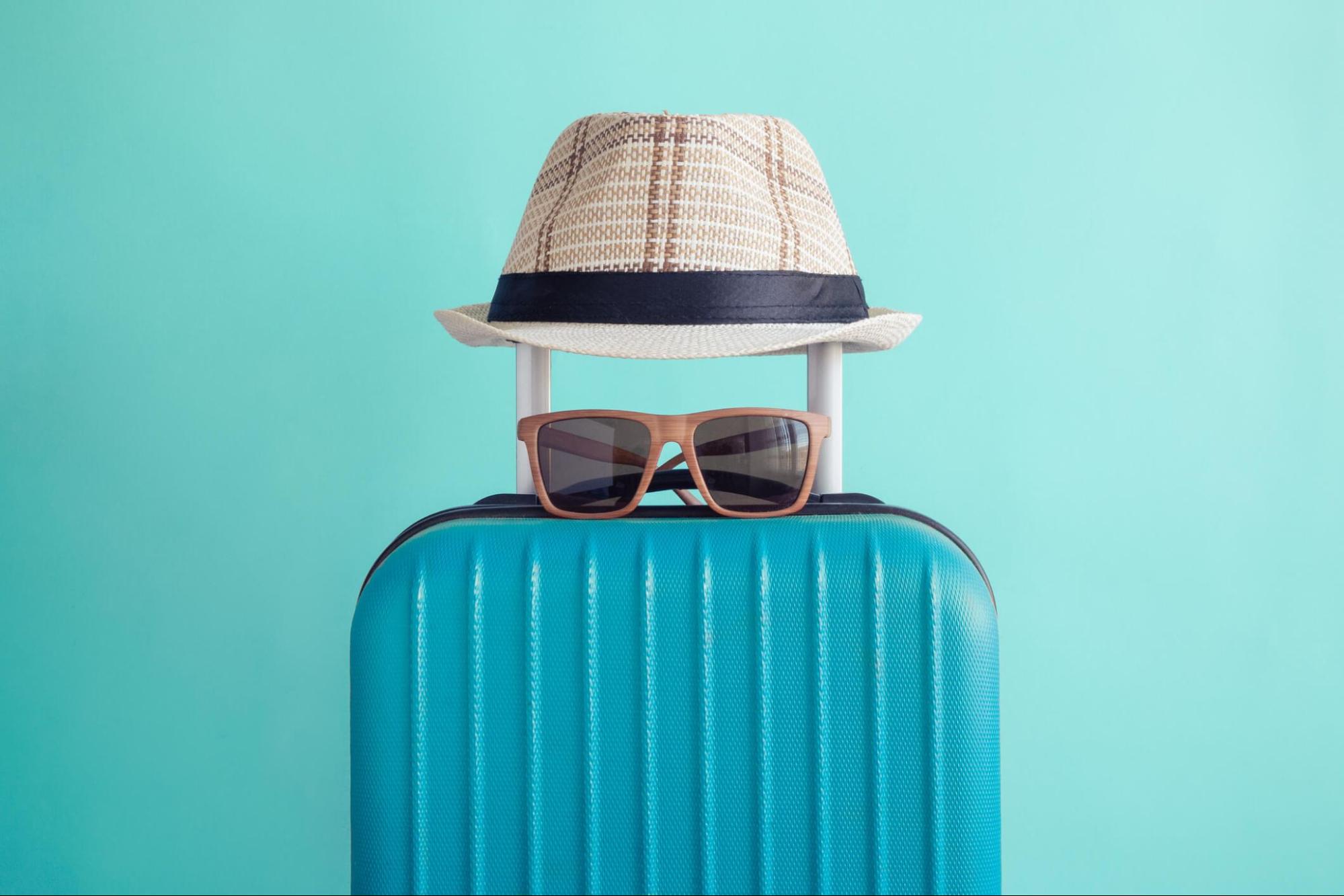 Sunglasses and a sun hat resting on a suitcase for a trip
