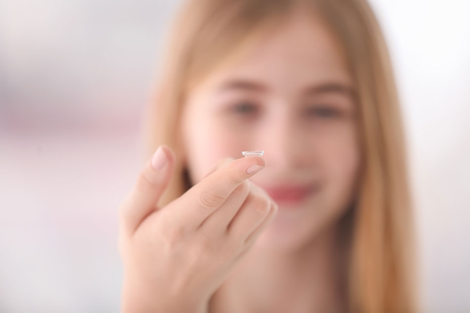teenage girl with contact lens on fingertip, blurred background