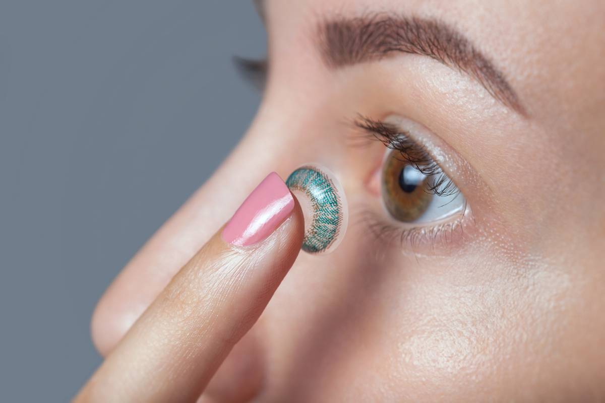 woman with brown eyes about to insert blue contact lens