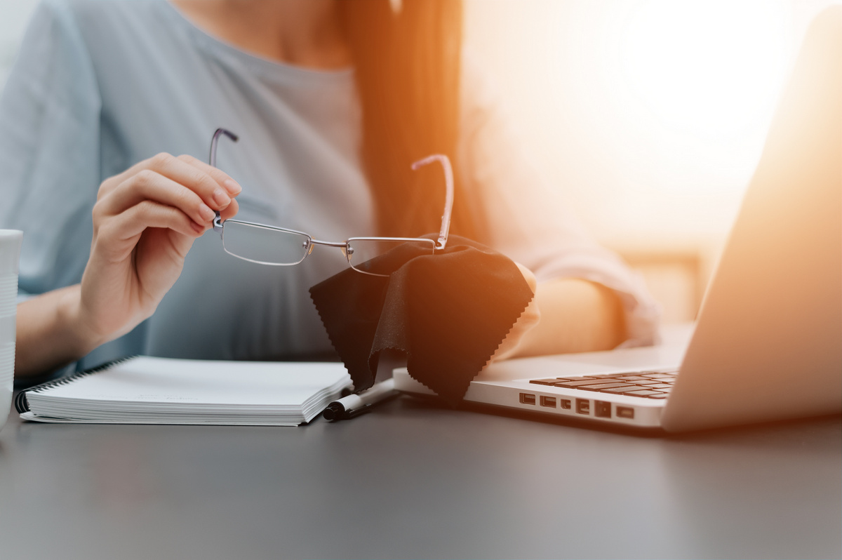 woman cleaning glasses in front of laptop