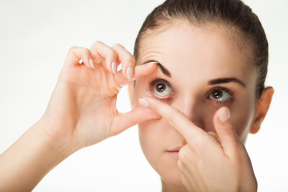 woman holding eye open while inserting contact lenses