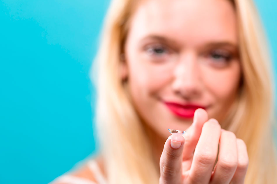 woman blurred in background happy and holding contact lens on tip of finger