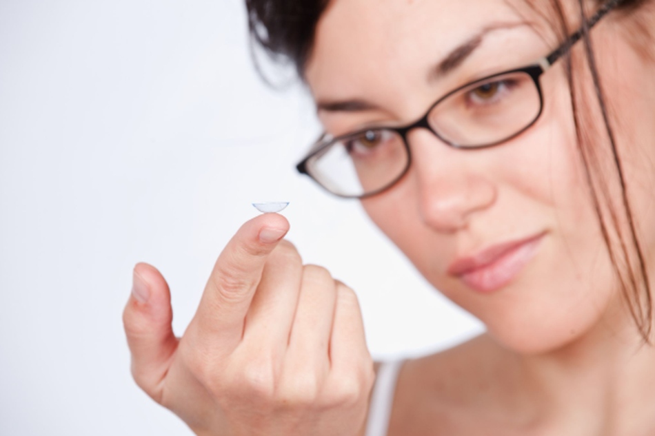 Woman wearing glasses while holding a contact lens on her fingertip