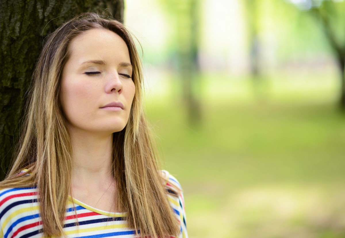 woman leaning against tree with eyes closed to relieve contact irritation