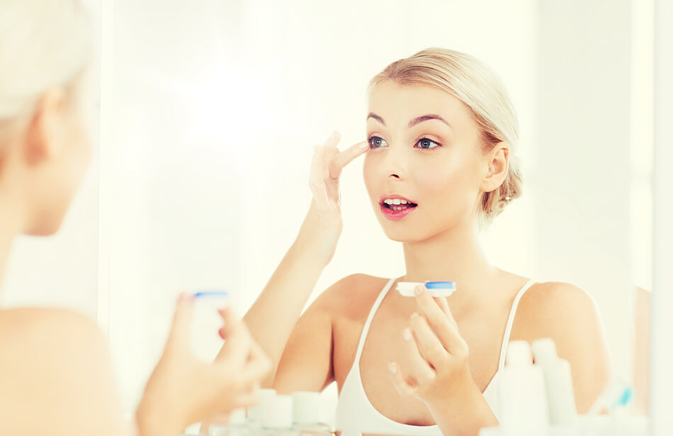 woman in mirror putting contacts in