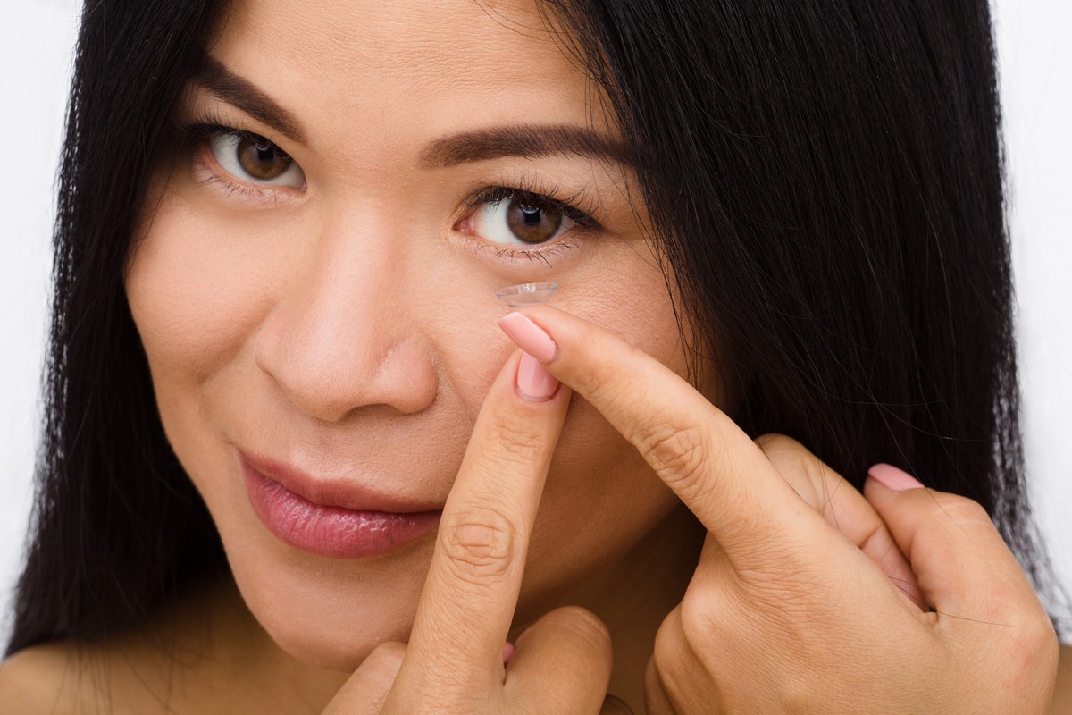 woman putting contact lens into her left eye