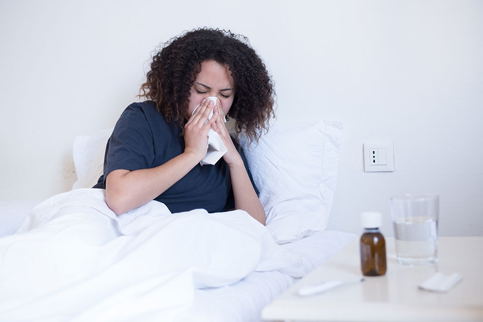 woman sick in bed blowing nose