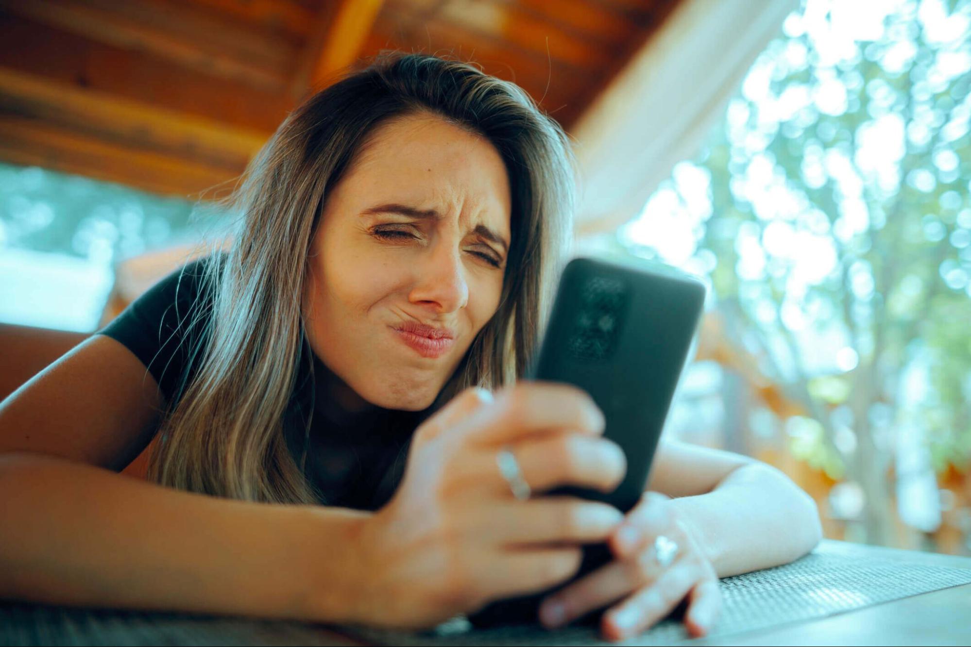 Woman squinting at a smartphone screen, a common sign of needing multifocal contact lenses.