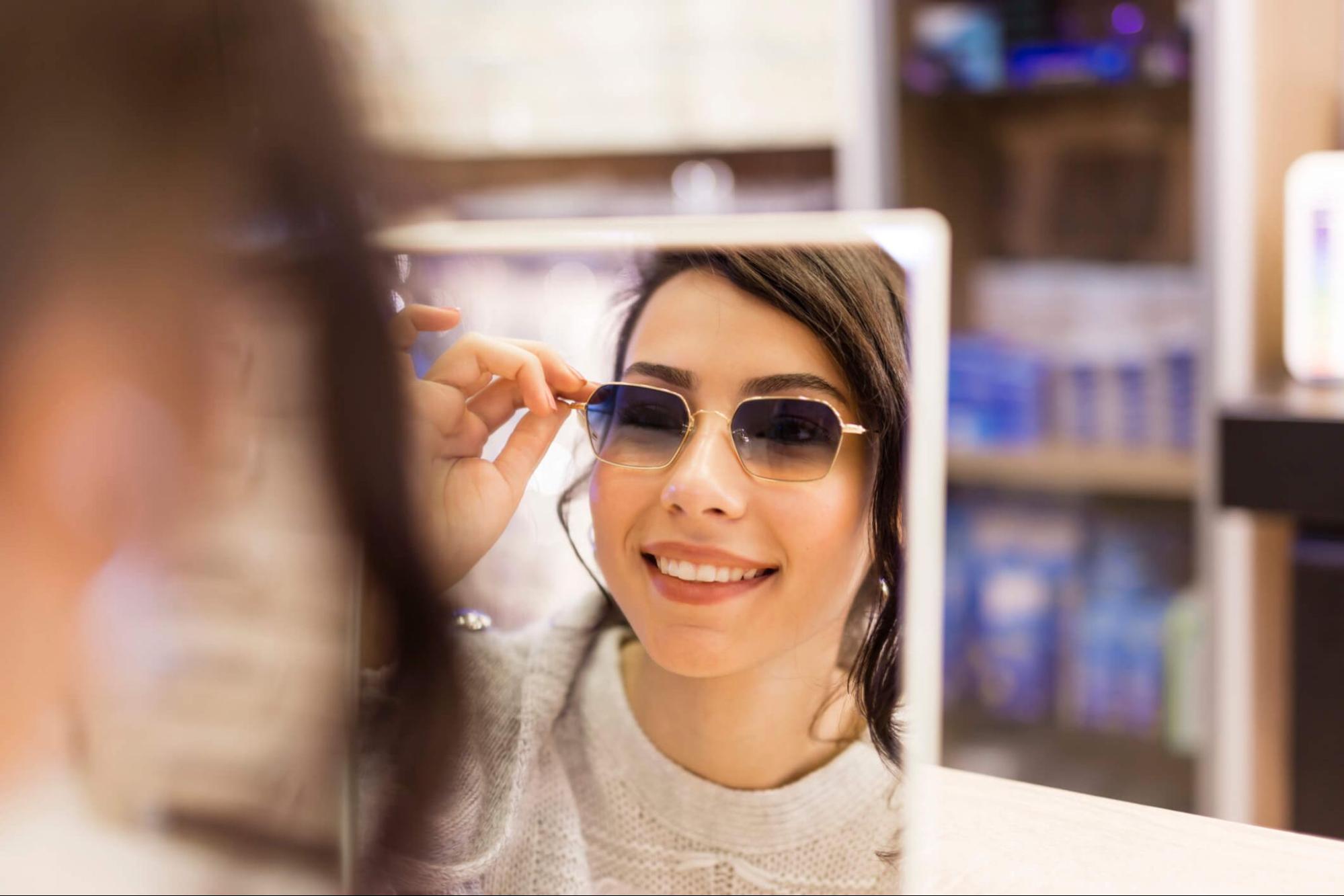 Woman trying on sunglasses with UV protection in store mirror