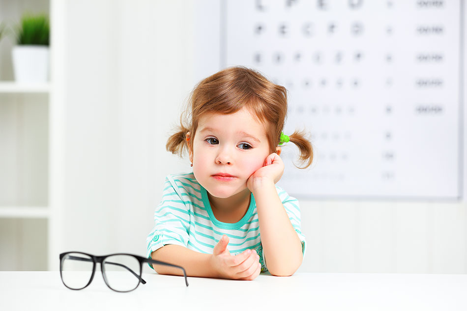 young child with glasses in front, eye chart in background