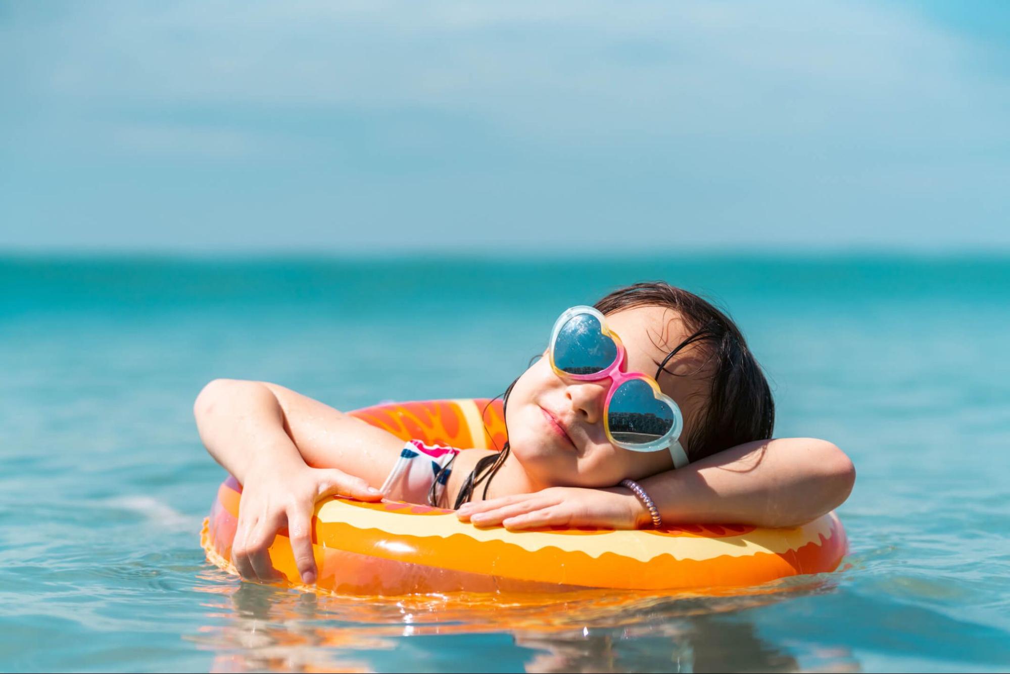 Young girl wearing heart-shaped sunglasses for kids floating on an inflatable ring in the ocean