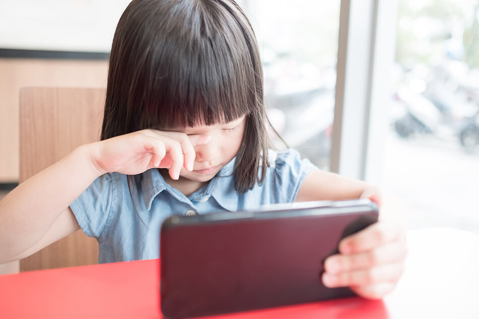 young girl rubbing eyes while holding a computer tablet