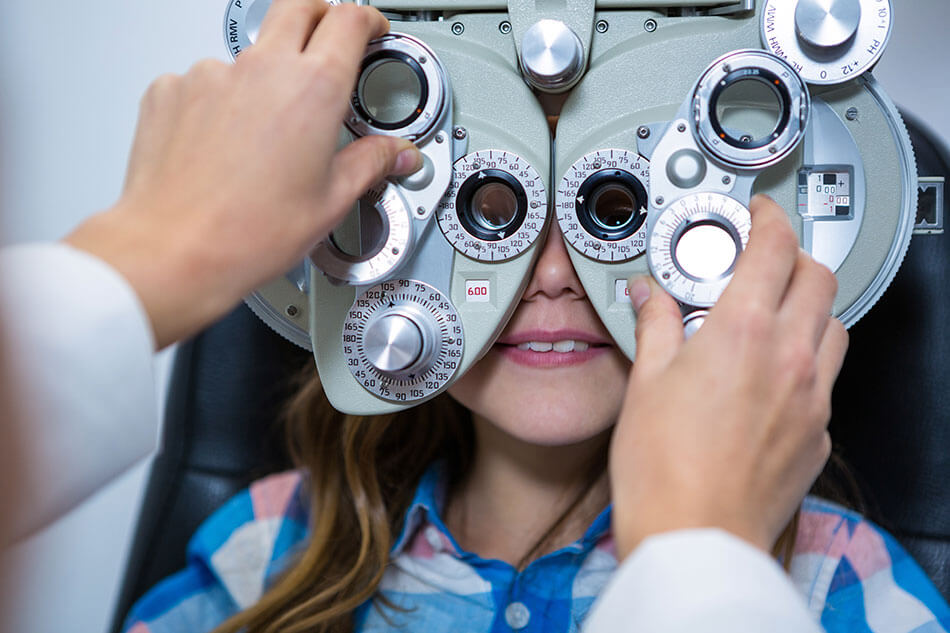 Female eye doctor examining a young girl’s eyes through a phoropter