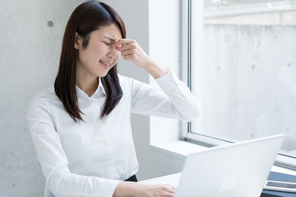 Young woman with contact lens irritation in front of laptop computer